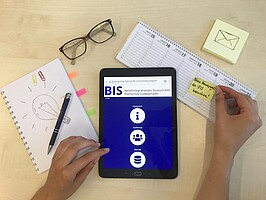 Symbolfoto: Schreibtisch mit Utensilien, ein Kalender, eine Brille und die Startseite der BIS Homepage auf einem Tablet stehen für ein gutes Zeitmanagement und den Durchblick, den man bei BIS braucht, um erfolgreich zu sein