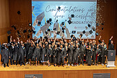 Graduates throw their graduate hats and confetti into the air on stage