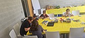 kinderzukunftsdiplom-ibe-2026 3 Kinder und 2 Frauen sitzen am Tisch und malen