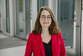 Portrait of a woman in her early 50s with long brown hair, glasses, and a red jacket