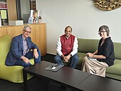 Three people are sitting on sofas in an office and smiling.
