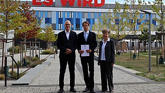 czs_Stiftungsprofessur_piller_woelfing_weber_dressler-HWG-2026er Ein älterer mann, ein jüngerer mann und eine ältere Frau stehen lächelnd vor dem Neubau