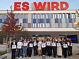 Größere Gruppe von Studierenden auf dem Campus der Hochschule mit Urkunden in der Hand 