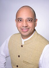 A smiling middle-aged man with a high forehead and a beige vest