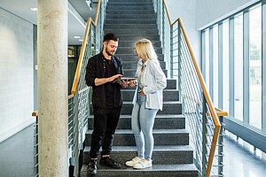 Zwei Studierende, die sich im Treppenhaus der Hochschule entspannt unterhalten