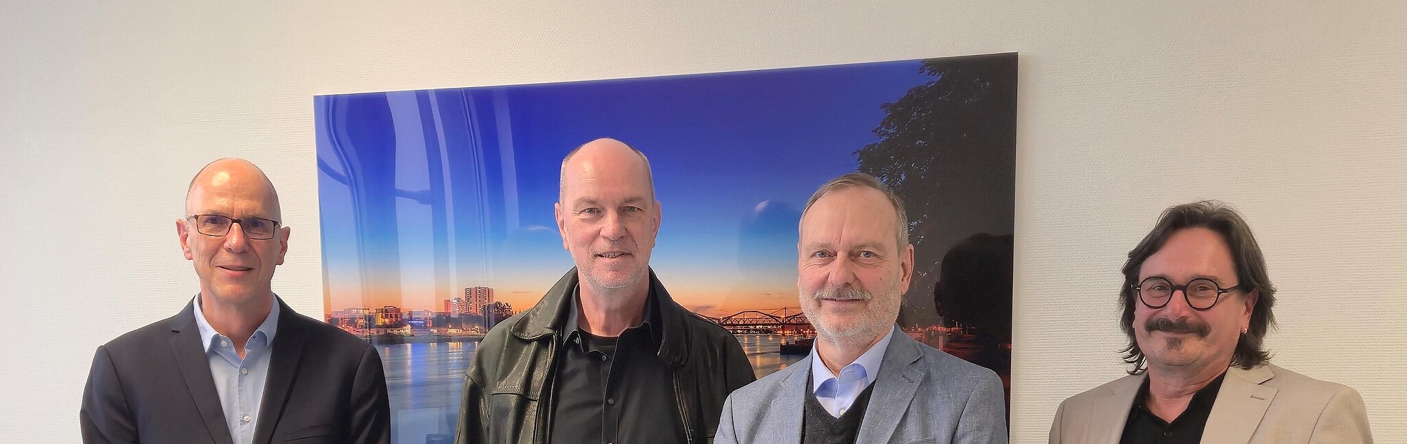 3 ältere Männer und ein Mann mittleren Alters stehen lächelnd in einem Büro
