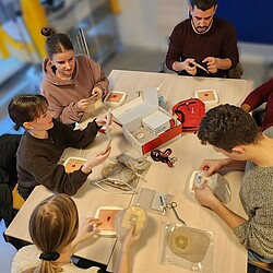 Eine Gruppe übt den Wechsel eines Stomas, auf einem Tisch liegen Übungsbeispiele und leere Stomabeutel.
