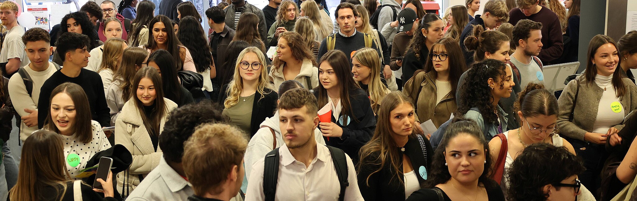 Junge Menschen warten geduldig in einer langen Schlange vor einem Gebäude.