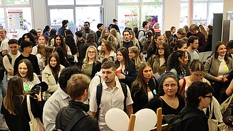 Junge Menschen warten geduldig in einer langen Schlange vor einem Gebäude.