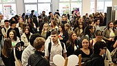 Junge Menschen warten geduldig in einer langen Schlange vor einem Gebäude.