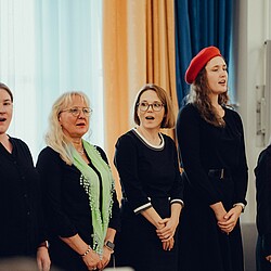 Five choristers singing together, one of them wearing a red beret and another a green scarf.