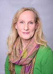 Porträtbild einer Frau mittleren Alters mit langen blonden Haaren, grünem Pulli und gemustertem Schal