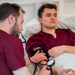 Übung zur Blutdruckmessung, ein Studierdender liegt dabei im Bett und übernimmt die Rolle das Patienten.
