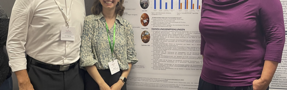 Three people stand in front of a scientific poster on research into humanoid robots and smile at the camera. The poster shows texts, diagrams and recommendations from several field studies.