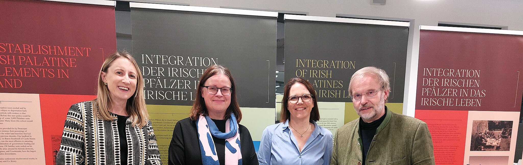 251117_Irische Pfälzer_Gruppenfoto Redner Gruppenfoto der vier Redner*innen vor der Plakatausstellung