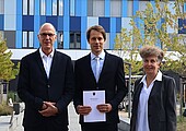 Ein älterer mann, ein jüngerer mann und eine ältere Frau stehen lächelnd vor dem Neubau