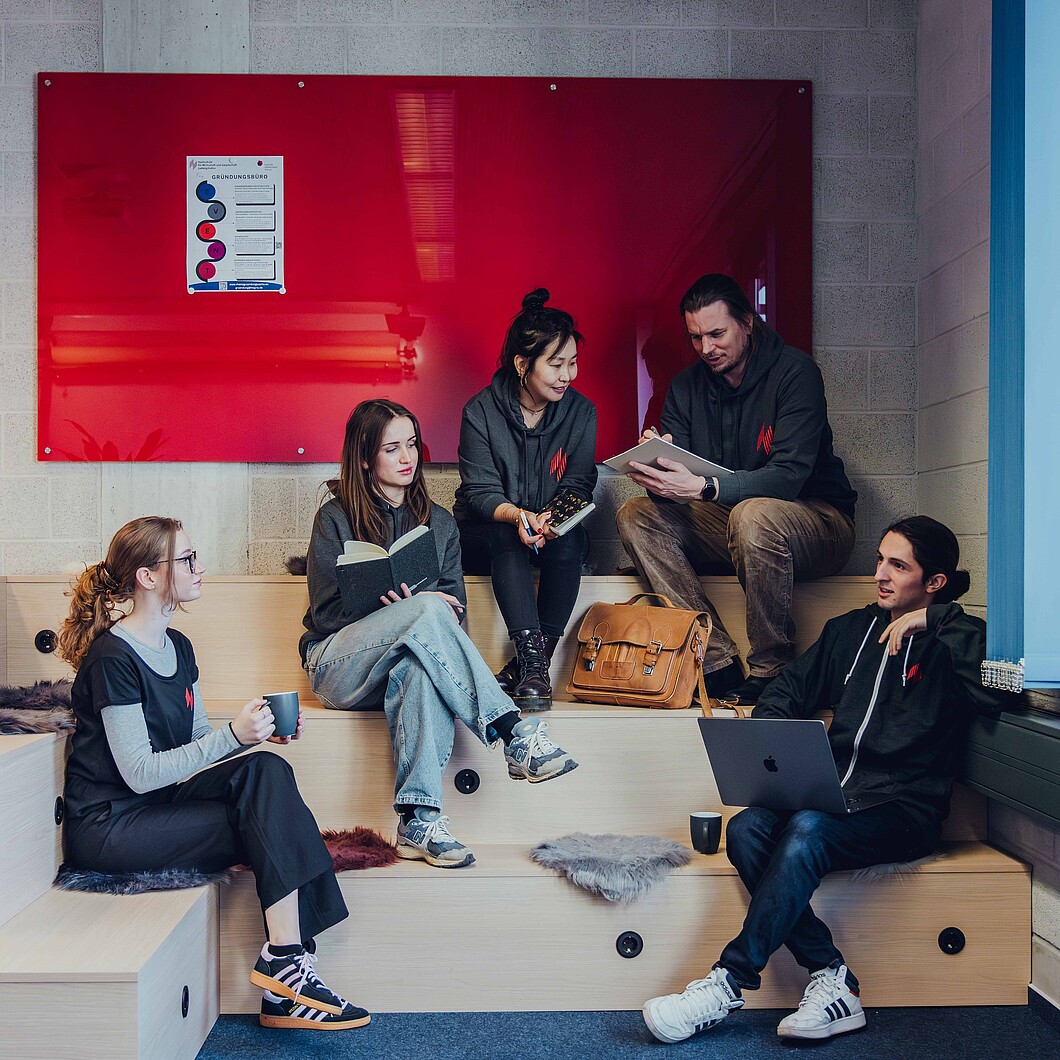 Studierende auf Sitztreppe mit roter Tafel im Hintergrund