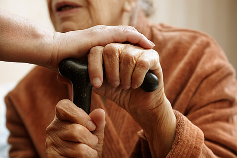 Alte Person mit Stock, bekommt eine helfende Hand gereicht.
