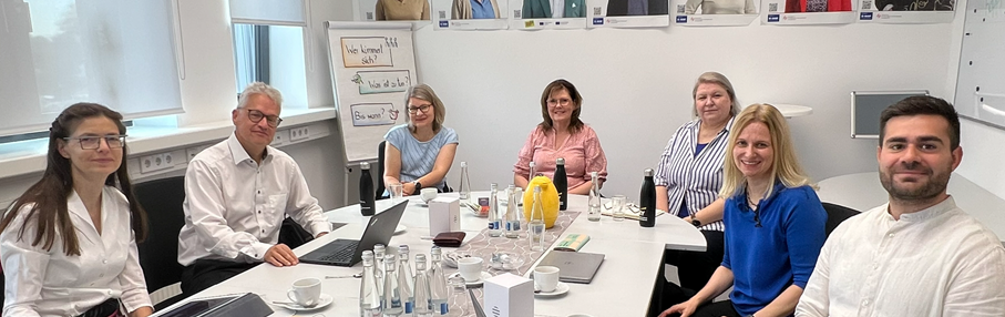 Sieben Personen sitzen um einen Tisch und arbeiten