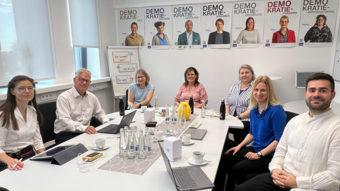 Sieben Personen sitzen um einen Tisch und arbeiten