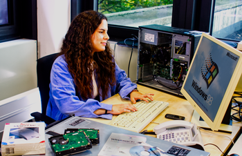 Picture shows young woman sitting at an outdated computer.