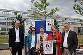 show_your_face_for_democracy_university_administration-HWG-2025 Two middle-aged men and three middle-aged women are standing on campus, smiling in front of posters for the photo campaign "Show Your Face for Democracy"